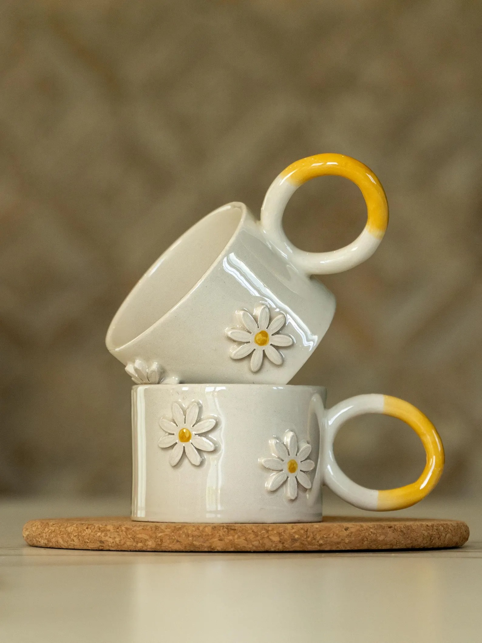 Pair of white ceramic mugs with a daisy relief and yellow handles