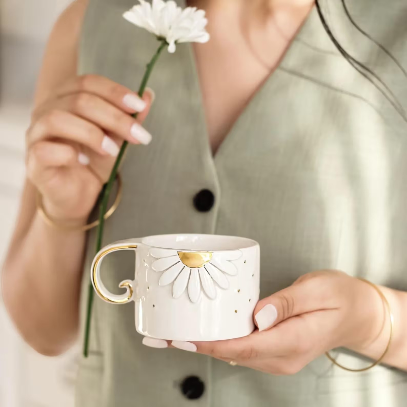 White ceramic cup with a daisy relief and gold detail held in hands