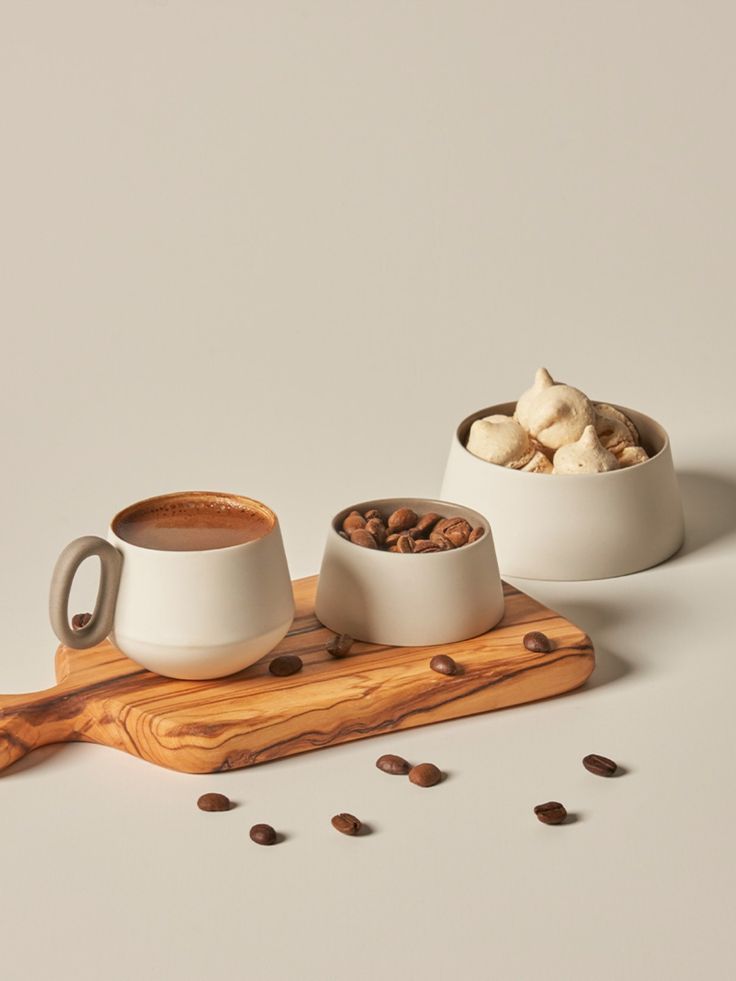 Matte cream ceramic cup and bowls on a wooden board with coffee beans
