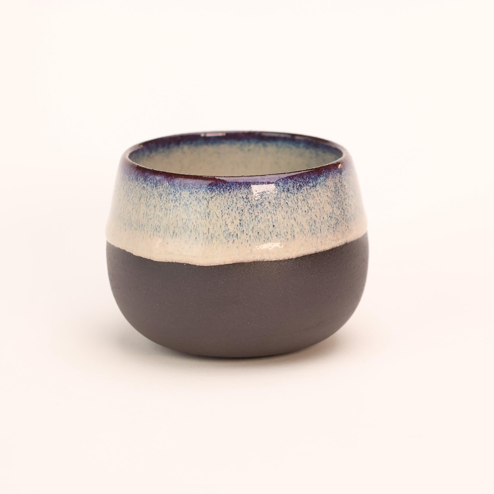 Ceramic cup with a blue and cream glaze fading into raw dark clay