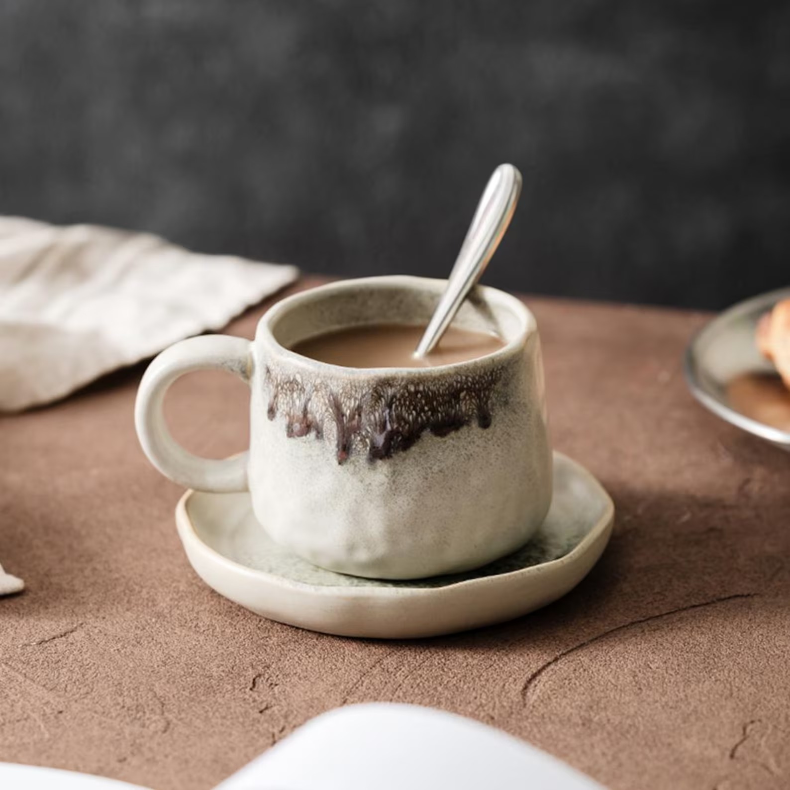 Cream ceramic cup with a brown drip glaze and a small saucer